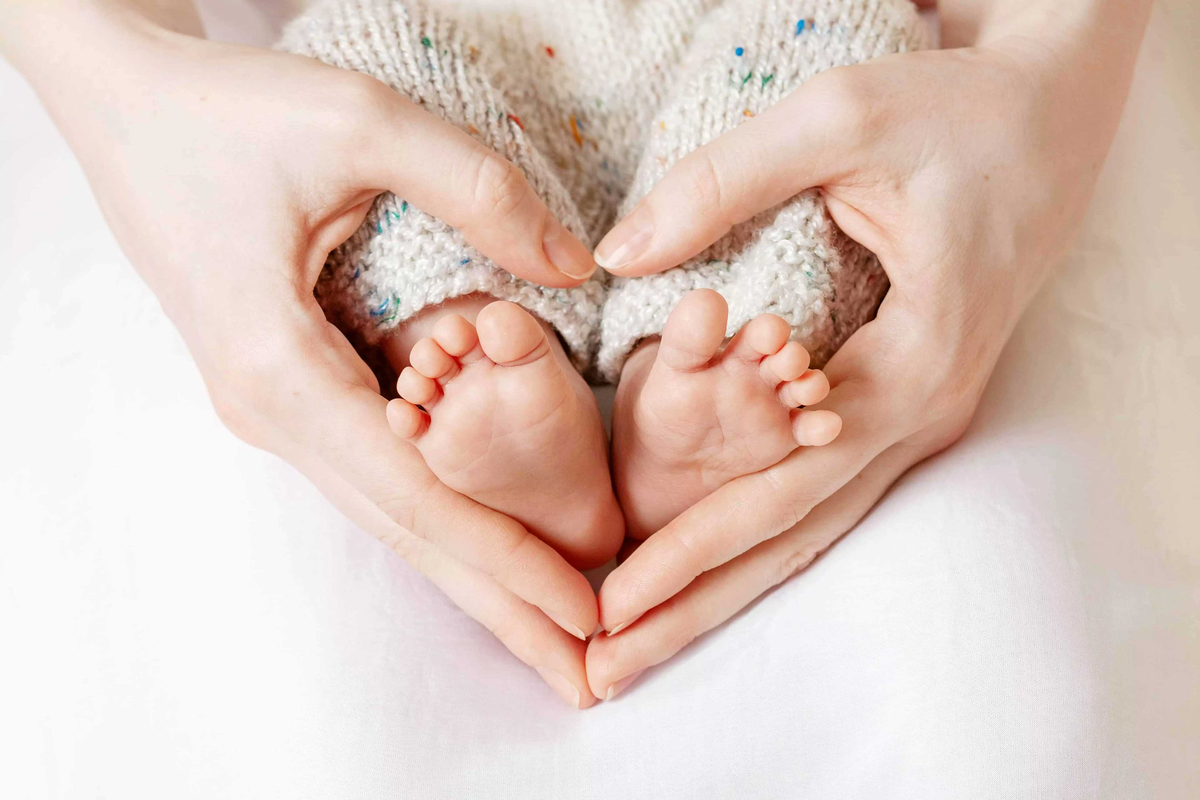 Pés de um bebê com duas mãos ao redor formando um coração.